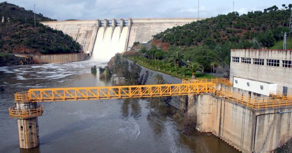 Barragem com comportas abertas e central hidroelétrica.